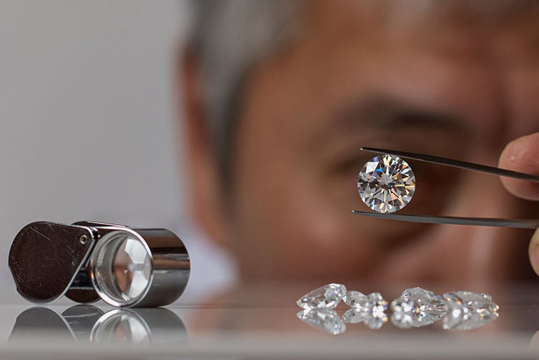 Un gemmologue avec un diamant rond Un gemmologue regarde à la loupe un diamant taille ronde avec un grossissement x10